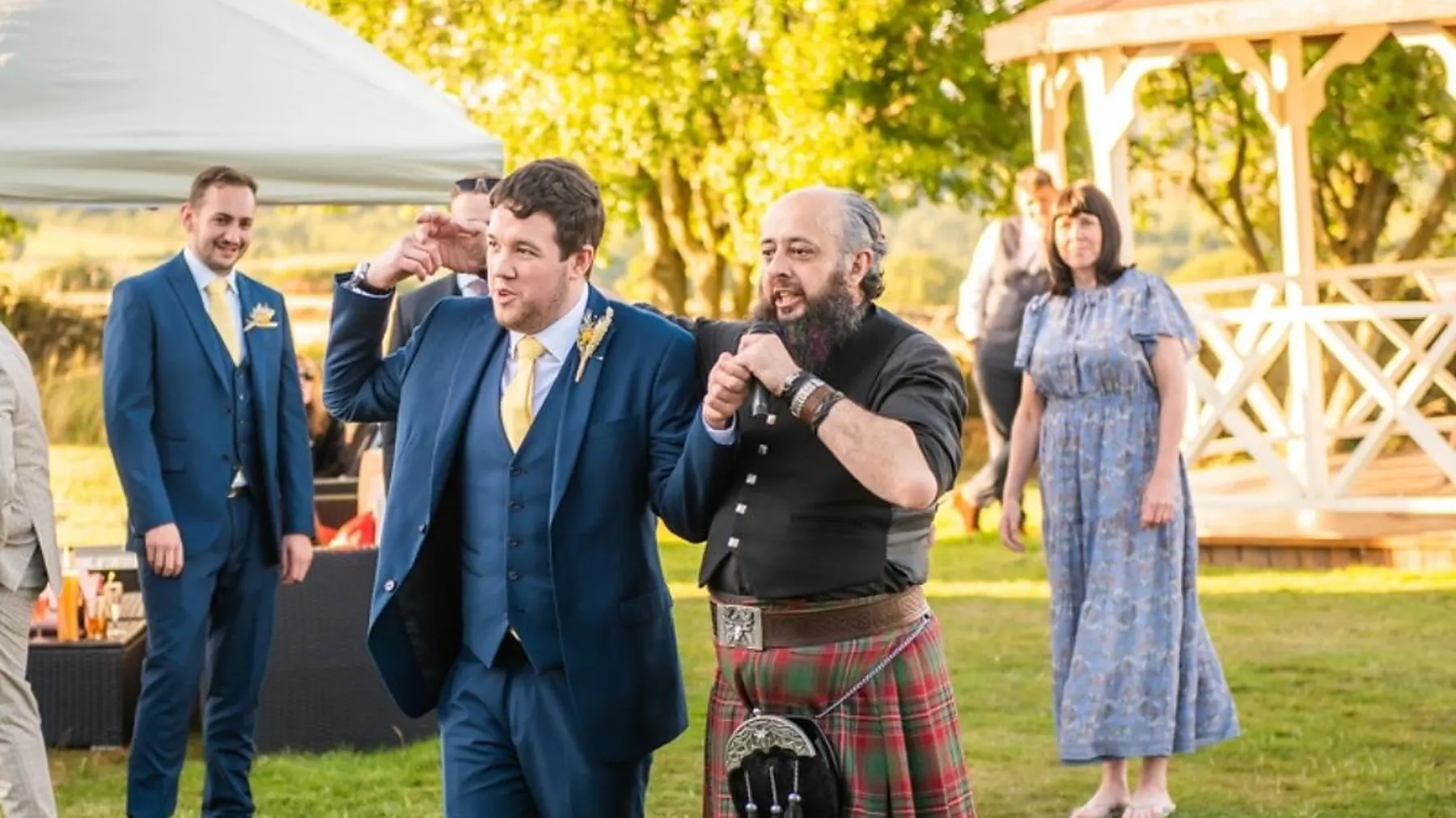 Schuggie calling a ceilidh beside a marquee as colleagues in suits join in