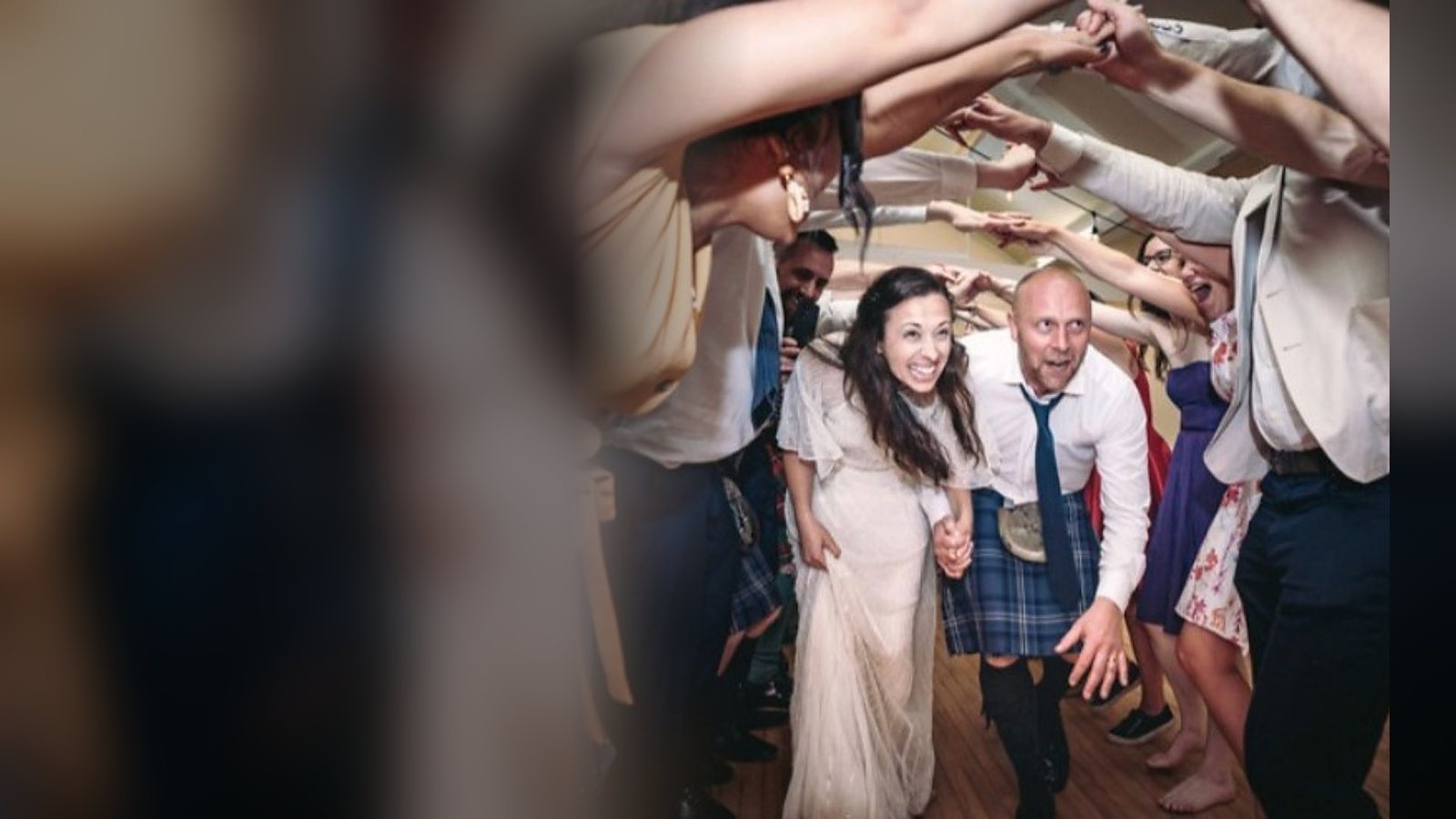 A couple ducking through an arch of raised hands during a ceilidh dance at their wedding