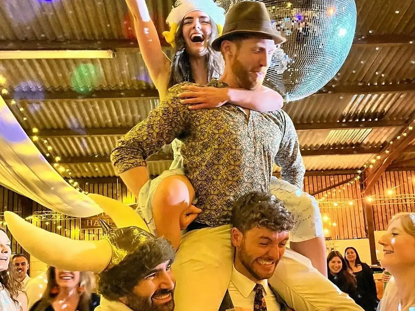 Party guests lifted on shoulders under a glitterball, mid-celebration