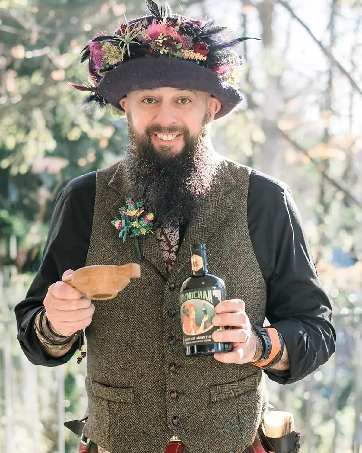 Schuggie in tweed waistcoat and flowered hat, raising a traditional Quaich friendship cup